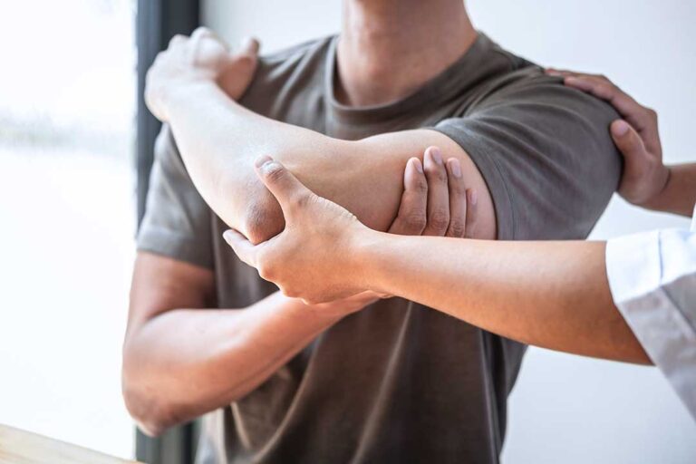 Person applying a wrapped cold pack to the lower back while seated at home.
