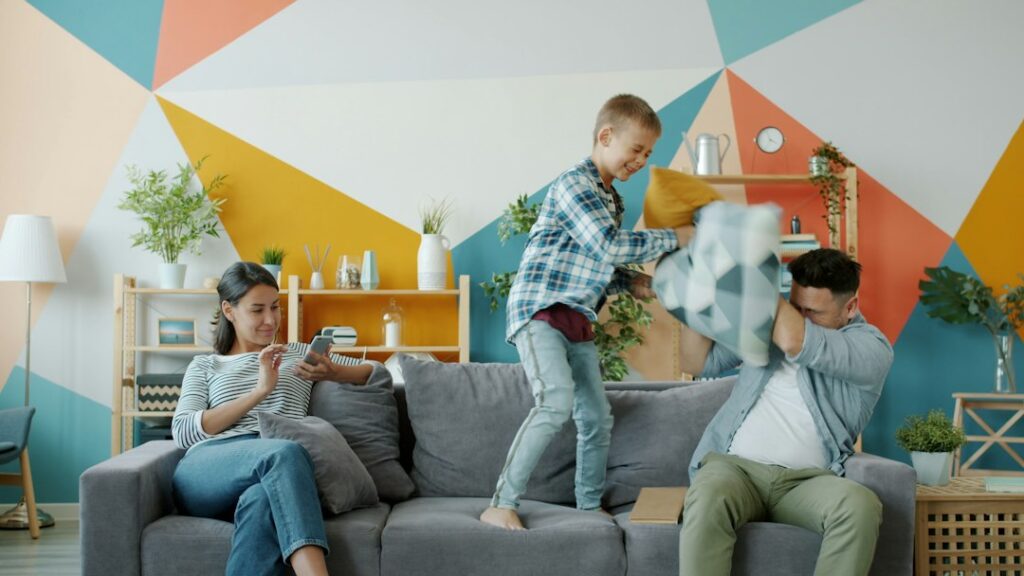 Parent and child stretch together in a bright living room beside sports equipment and comfortable exercise clothing.