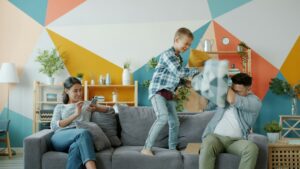 Parent and child stretch together in a bright living room beside sports equipment and comfortable exercise clothing.